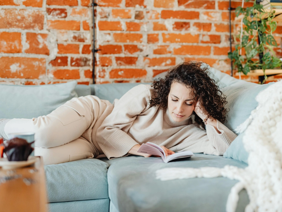 Frau macht Digital Detox und liegt auf der Couch, während sie ein Buch liest