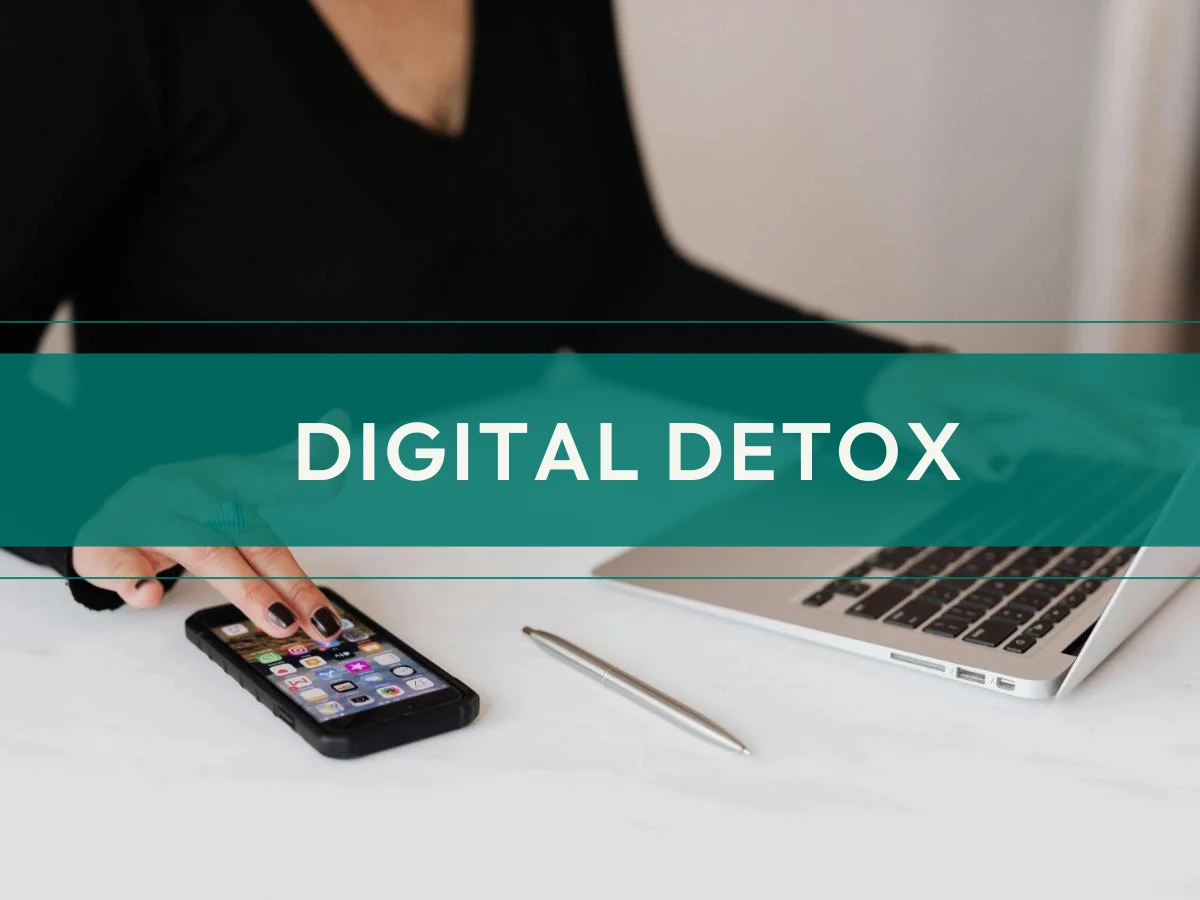 Digital Detox Schriftzug über Zuschnitt einer Frau, die am Schreibtisch sitzt mit Smartphone und Laptop