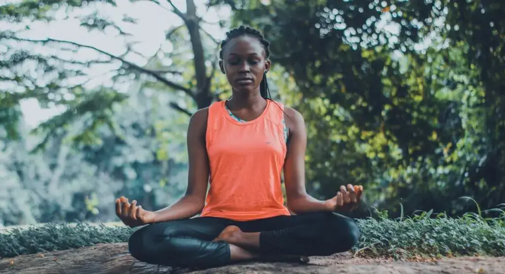 Ein Mädchen aus Indien, die draußen in der Mutter Natur auf dem Boden sitzt und Yoga praktiziert.